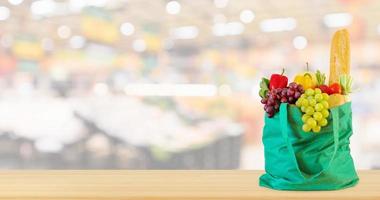 fruits et légumes frais dans un sac à provisions vert réutilisable sur une table en bois avec supermarché épicerie arrière-plan flou défocalisé avec lumière bokeh photo