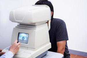 jeune bel homme asiatique passer un examen de la vue avec une machine de test optique de la vue photo