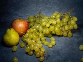 une grosse grappe de raisin avec une pomme et une poire sur fond noir. raisins husaini. photo