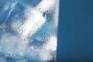 glaçons dans un verre avec de l'eau glacée rafraîchissante sur fond bleu. photo
