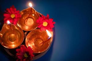 joyeux Diwali. célébrant la fête indienne de la lumière. lampes à huile traditionnelles diya et fleurs rouges sur fond bleu photo