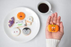 main de femme tenant un biscuit d'halloween drôle en buvant du café. bonne fête d'halloween, astuce ou menace, bonjour octobre, automne automne, concept traditionnel, fête et vacances photo