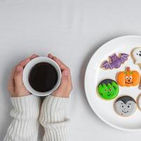 main de femme tenant une tasse de café en mangeant des biscuits d'halloween drôles. bonne fête d'halloween, astuce ou menace, bonjour octobre, automne automne, concept traditionnel, fête et vacances photo