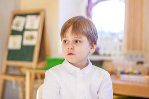 élégamment vêtu d'une chemise blanche, un petit garçon est assis dans la salle de classe pour les cours. portrait d'un garçon photo