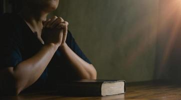 main de personne de prière sur fond noir. une femme catholique chrétienne prie Dieu dans le noir à l'église. fille croit et foi en jésus christ. la religion du christ et le christianisme adorent ou prient le concept. photo