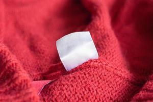 étiquette de vêtements de soin de lessive blanche vierge sur fond de texture tricotée rouge photo