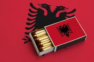 le drapeau de l'albanie est affiché dans une boîte d'allumettes ouverte, qui est remplie d'allumettes et repose sur un grand drapeau photo