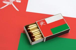 le drapeau d'oman est affiché dans une boîte d'allumettes ouverte, qui est remplie d'allumettes et repose sur un grand drapeau photo