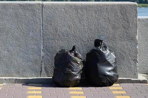 Deux sacs à ordures noirs sur le sol carrelé de la rue à la clôture en béton de la ville photo