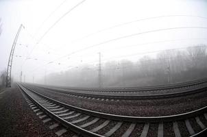 la voie ferrée par un matin brumeux. beaucoup de rails et de traverses vont dans l'horizon brumeux. photo fisheye avec distorsion accrue