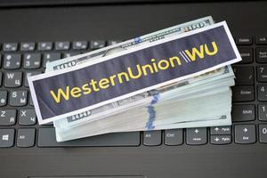 ternopil, ukraine - 6 septembre 2022 le logotype du papier western union se trouve sur un ordinateur portable noir avec des billets en dollars américains. western union company est une multinationale américaine de services financiers photo