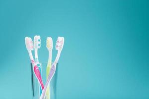 brosses à dents de différentes couleurs dans un verre transparent sur fond bleu. photo