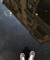 reflet dans une flaque d'eau d'un immeuble et les jambes d'un homme en baskets. photo