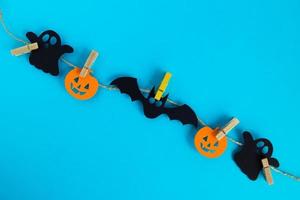 préparation pour halloween. décorations en papier noir et orange - fantômes, citrouilles et chauves-souris sur une corde avec des épingles sur fond bleu avec espace de copie. photo