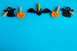 préparation pour halloween. décorations en papier noir et orange - fantômes, citrouilles et chauves-souris sur une corde avec des épingles sur fond bleu avec espace de copie. photo