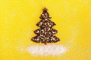 arbre de noël à base de grains de café et d'étoile d'anis décorée, saupoudrage culinaire multicolore et copeaux de noix de coco sur fond jaune, vue de dessus. photo