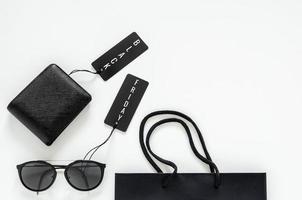 mise à plat d'étoffes pour hommes - portefeuille noir, lunettes de soleil, étiquettes de prix et sac à provisions sur fond blanc pour le concept de vente du vendredi noir. photo