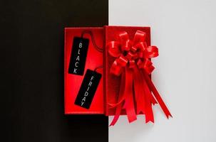 boîte de noël rouge avec ruban arc rouge et étiquette de prix noire sur fond noir et blanc. notion de vendredi noir. photo