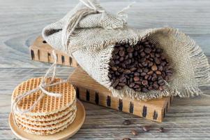 grains de café arabes ruast en toile de jute avec pile de gaufres hollandaises sur table en bois.