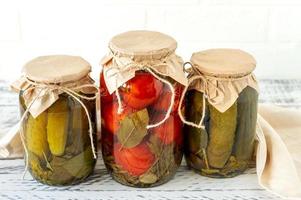 Conserves de tomates et de concombres faits maison dans un bocal en verre sur fond de bois photo