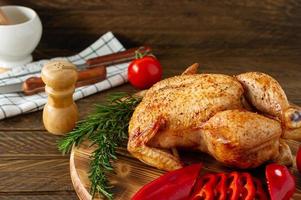 poulet entier rôti sur une planche en bois servi avec des légumes frais et des herbes. photo