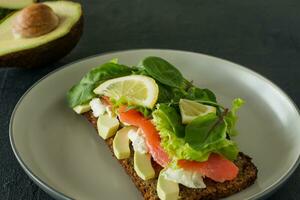 sandwich au fromage à pâte molle au saumon fumé, treillis et avocat. concept pour un repas savoureux et sain. nourriture sur une assiette. photo