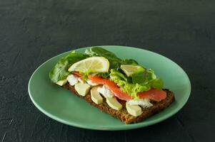 sandwich au fromage à pâte molle au saumon fumé, treillis et avocat. concept pour un repas savoureux et sain. nourriture sur une assiette. photo