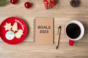 Objectif 2023 avec carnet, tasse à café noire, biscuits de noël et stylo sur table en bois. noël, bonne année, résolution, liste de choses à faire, concept de stratégie et de plan photo