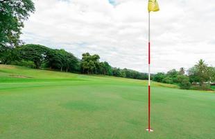 terrain de golf avec paysage de gazon vert. champ d'herbe verte avec mât de drapeau de golf jaune. terrain de golf à l'hôtel ou au centre de villégiature. paysage de terrain de golf avec ciel bleu et arbres verts. terrain de sport vert. photo