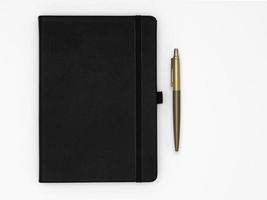 cahier noir fermé et stylo doré à côté sur fond blanc photo