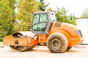 rouleau d'asphalte orange sur le parking avant le début des travaux de construction sur la pose de bitume. machine pour le compactage de matériaux de construction en vrac. photo