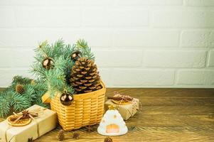 composition festive de noël sur une table en bois. panier en osier avec un grand cône de cèdre, des branches d'épinette, des cadeaux et une bougie chaude. photo