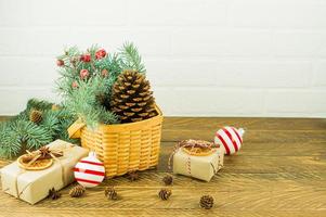 décoration festive pour la maison à noël. panier en osier avec branches et baies d'épinette, cône de cèdre et coffrets cadeaux sur une table en bois. photo