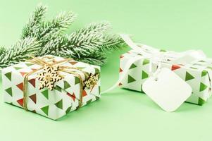 cadeaux emballés dans du papier festif sur fond vert avec une branche d'épinette dans la neige. décoré de flocons de neige. carte de félicitations. photo