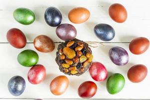 beau fond festif pour les vacances de pâques. gâteau fait maison avec des fruits secs et des noix et des œufs peints sur une table en bois blanche. vue de dessus. photo