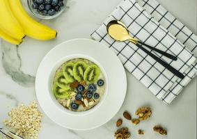 petit-déjeuner sain. bouillie d'avoine avec kiwi, myrtilles et noix dans un bol blanc sur un comptoir en marbre. flocons d'avoine, bananes mûres. vue de dessus. photo