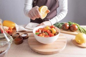 cuisiner des repas diététiques à la maison. la main d'une fille presse le jus de citron dans une salade de légumes en tranches dans un bol. photo