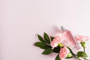 joli parfum féminin dans un flacon pulvérisateur en verre sur fond rose avec des œillets. vue de dessus, une copie de l'espace pour votre texte. photo