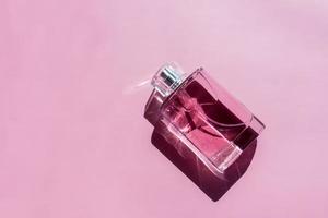 une bouteille de parfum ou d'eau de toilette en verre rose sur fond violet avec de belles ombres. vue de dessus. une copie de l'espace. photo