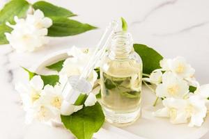 une bouteille ouverte avec un compte-gouttes d'huile de jasmin bio cosmétique sur fond de fleurs pour les soins de la peau du visage et du corps. relaxation. phytothérapie. photo