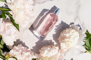 vue de dessus d'une bouteille transparente au parfum floral de parfum féminin ou d'eau de toilette. couper de belles pivoines et fond de marbre. photo