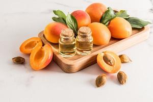 deux bouteilles en verre avec un bouchon en liège contenant de l'huile de noyau d'abricot biologique se tiennent sur un plateau en bois d'abricots juteux. un soin naturel révélateur. photo