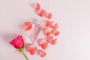 une bouteille d'eau de toilette ou de parfum d'un arôme délicat sur fond rose avec un bourgeon et des pétales de rose. vue de dessus. style plat. photo