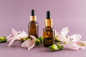 huile cosmétique, huile essentielle ou sérum d'auto-soin dans deux bouteilles sur fond violet avec des fleurs fraîches. cosmétiques naturels. photo