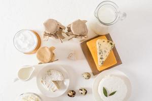 vue de dessus du fond blanc avec divers produits laitiers - lait en bouteilles, crème sure, fromage cottage dans le bol, fromage sur une planche de bois. photo