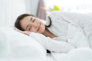 belle femme asiatique allongée sur le lit avec des oreillers confortablement soutenus. et souriant joyeusement photo