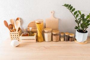 fond de cuisine blanc élégant avec des ustensiles de cuisine sur un comptoir en bois contre un mur texturé avec des plantes vertes. photo