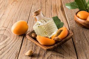 une bouteille en verre avec un couvercle en liège avec de l'huile de noyau d'abricot se trouve dans un bol en bois avec des abricots mûrs. soin antioxydant, rajeunissement. photo