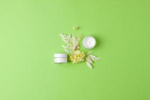 pots de crème cosmétique avec des fleurs sur fond vert. mise à plat, espace de copie photo