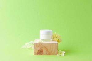 pot de crème cosmétique avec podium en bois et fleurs sur fond vert. gros plan, espace de copie photo